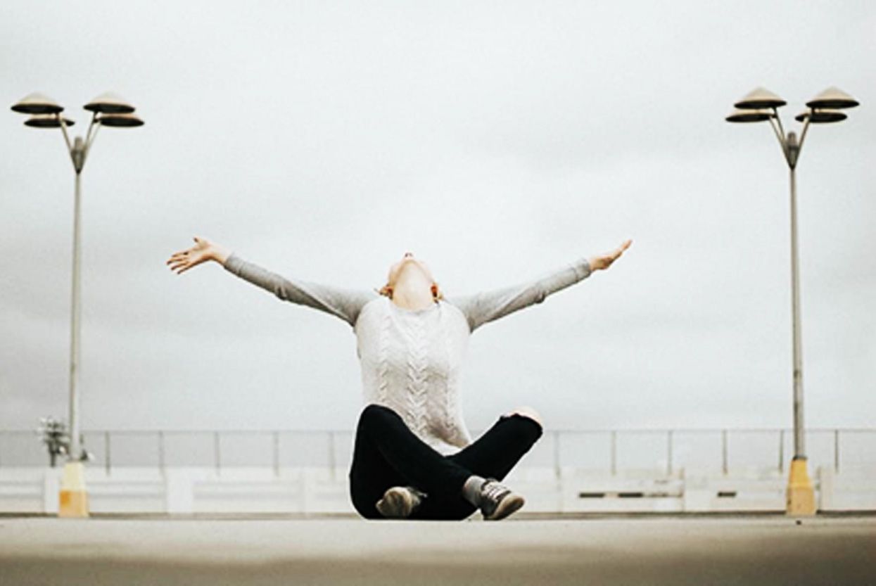 A woman is sitting on the ground with her arms outstretched.