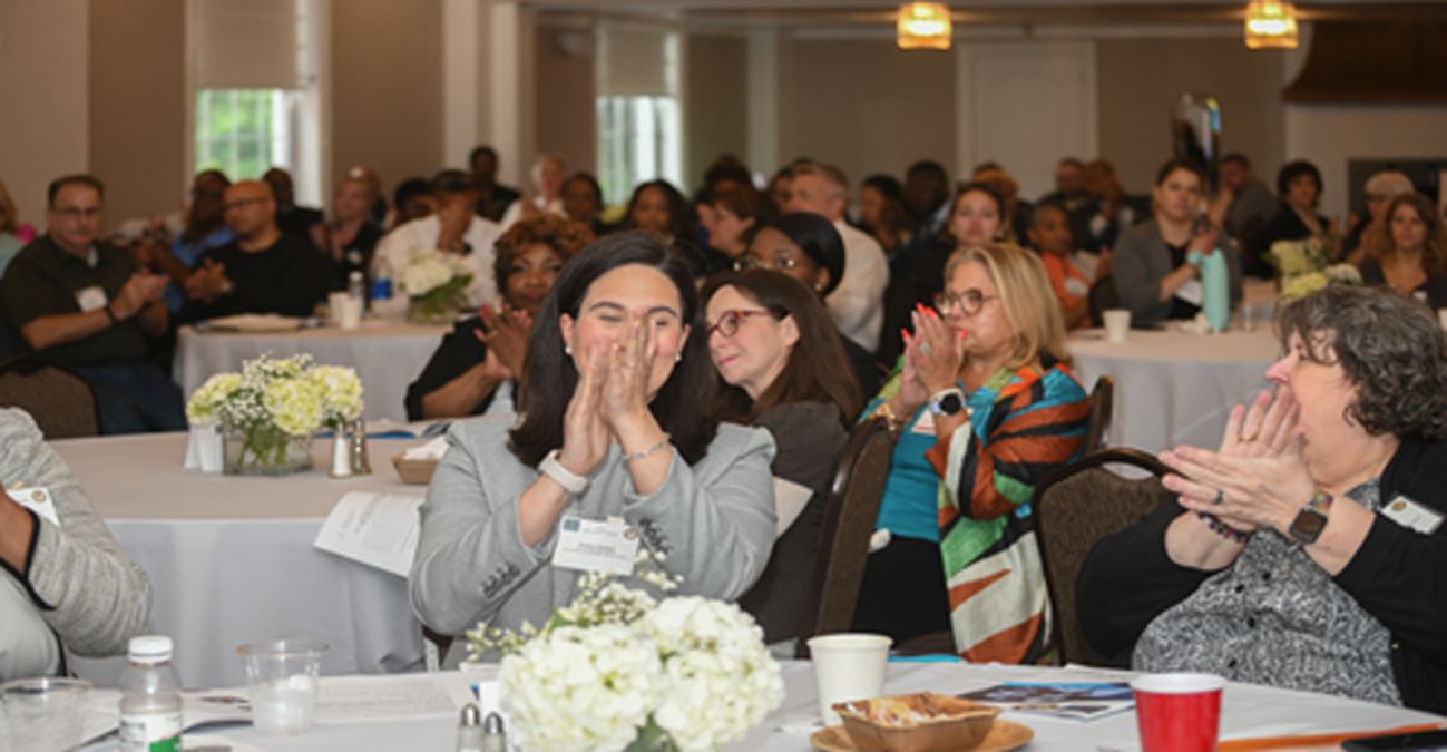 A group of people are sitting at tables in a room applauding.