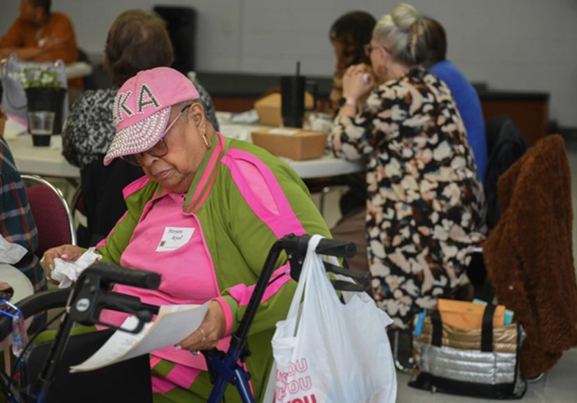 A woman in a pink hat is sitting in a wheelchair looking at papers.