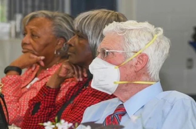 A man and two women wearing face masks are sitting at a table.