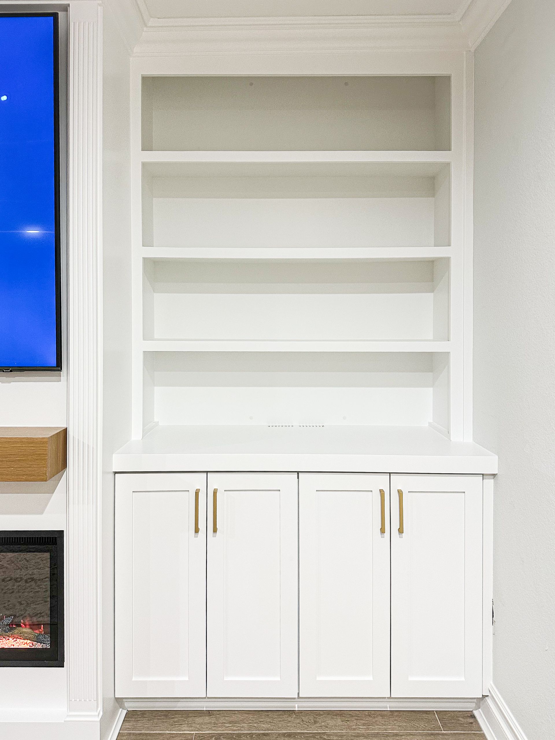 White built-in shelving and cabinet unit with gold handles in a bright room
