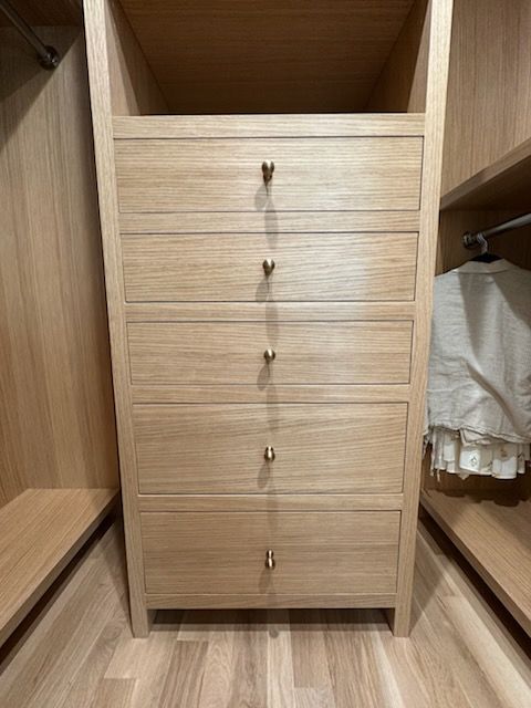 Wooden closet with five drawers centered between hanging sections in a walk-in wardrobe.