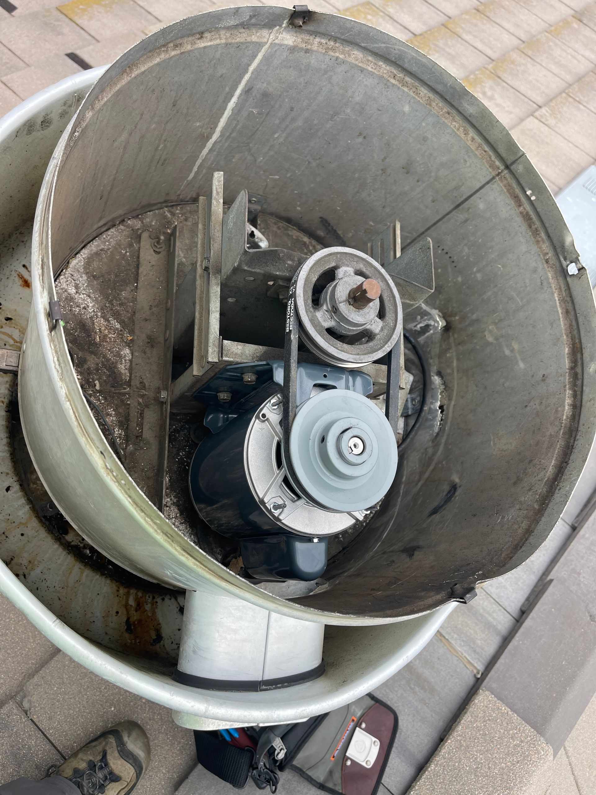 Overhead view of an industrial fan, showing motor, belts, pulleys, and inner components, likely on a rooftop.
