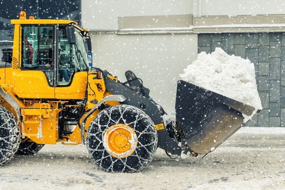 Yellow front loader pushing snow in a snowy industrial lot