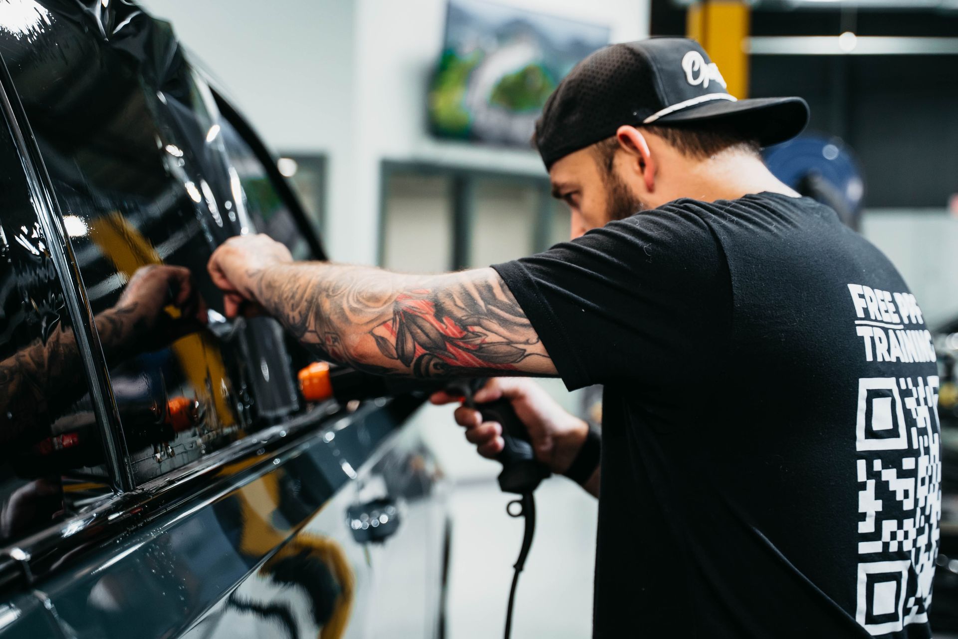 Man tattooing a car panel in a workshop, wearing a black cap and T-shirt