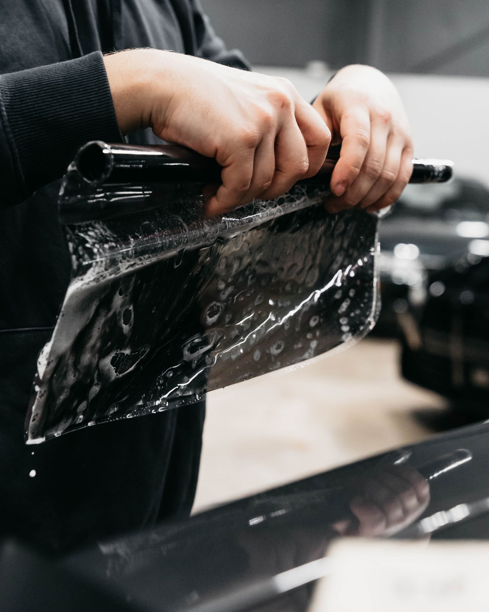 Hand washing the windshield of a black car in a garage, with water droplets visible