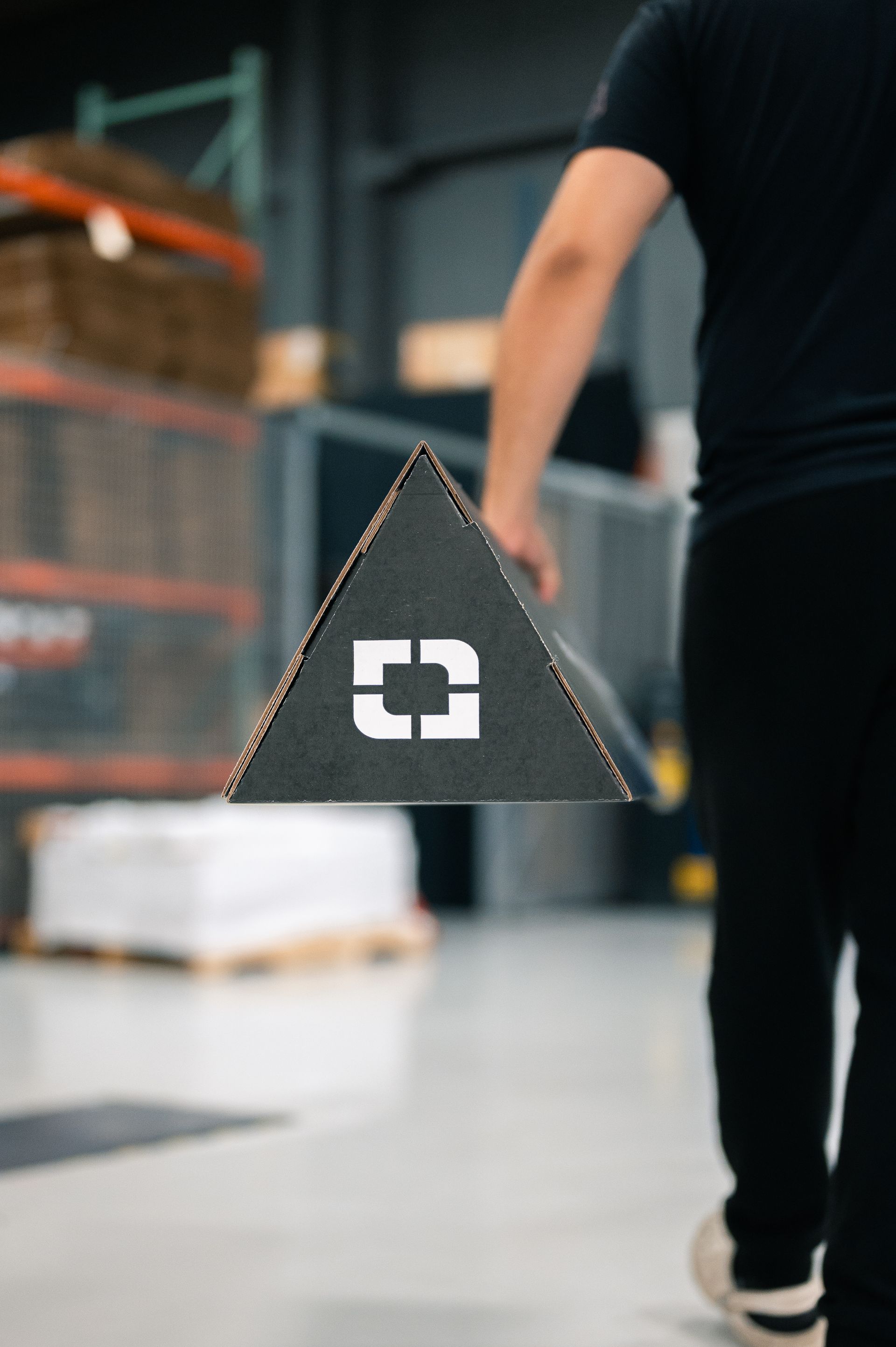 Person walking in a warehouse holding a black triangular sign with a white symbol