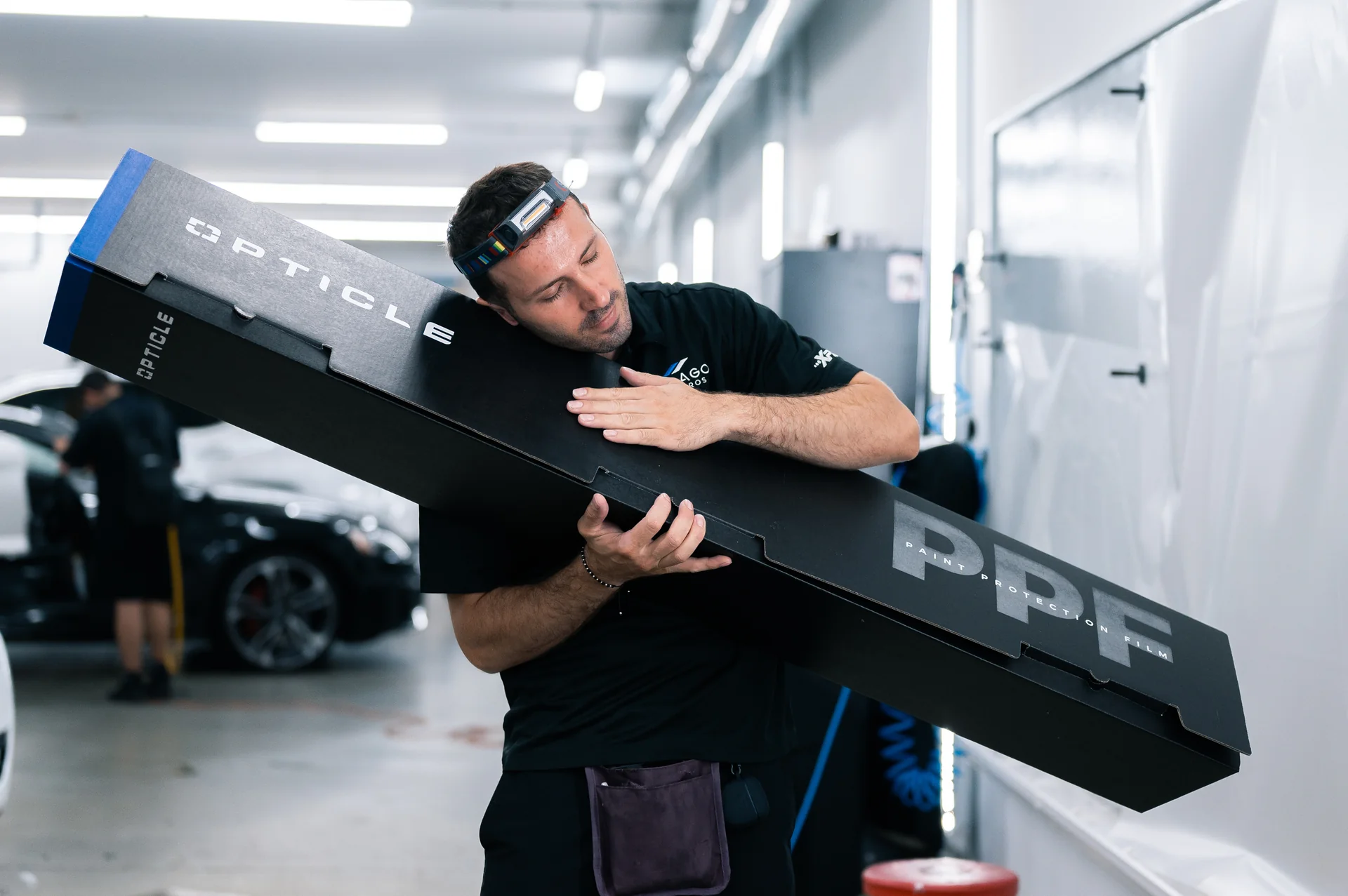 A man is carrying a large black box in a garage.