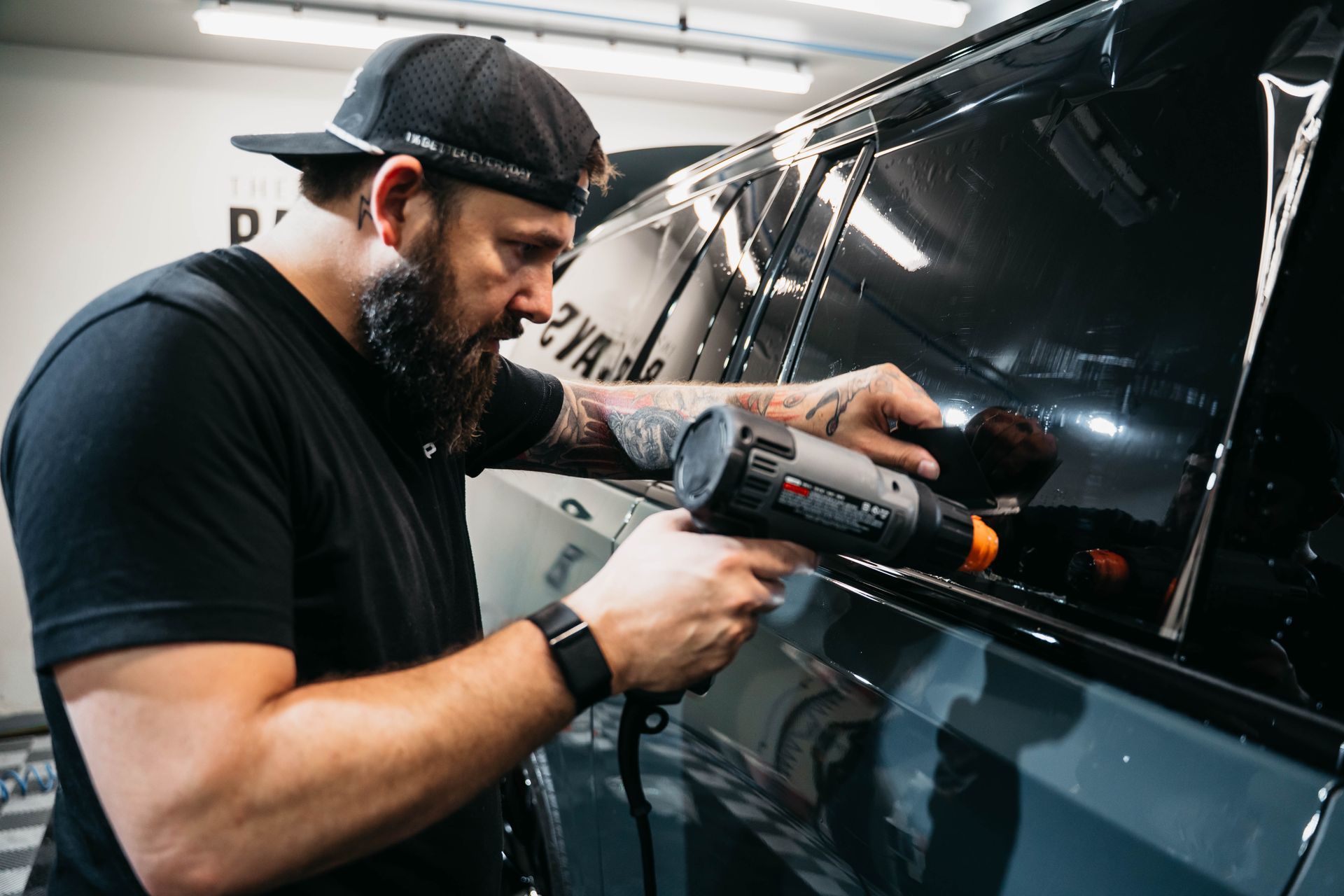 A person is applying a protective film to a black car.