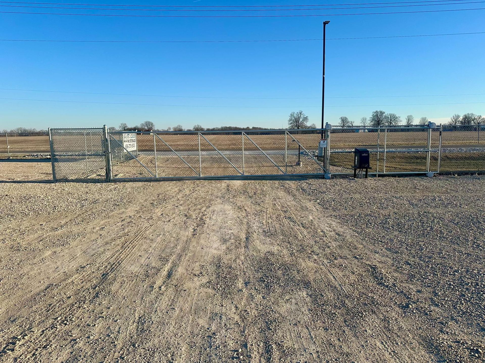 A gravel road leading to a fenced gate and a field under a clear blue sky.