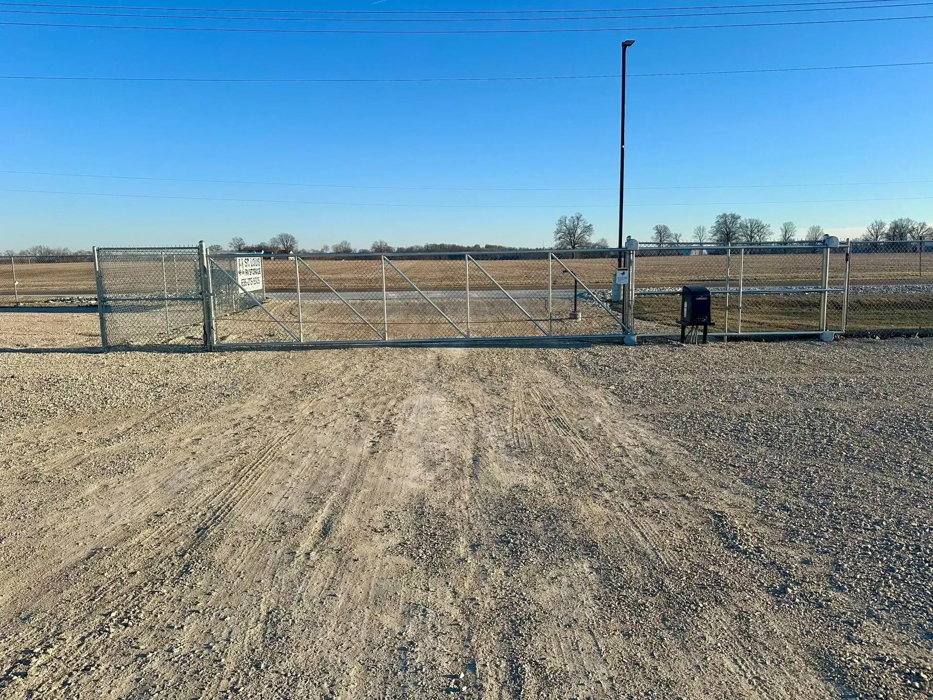 A closed chain-link security gate protecting the entrance to a gravel trailer storage area.