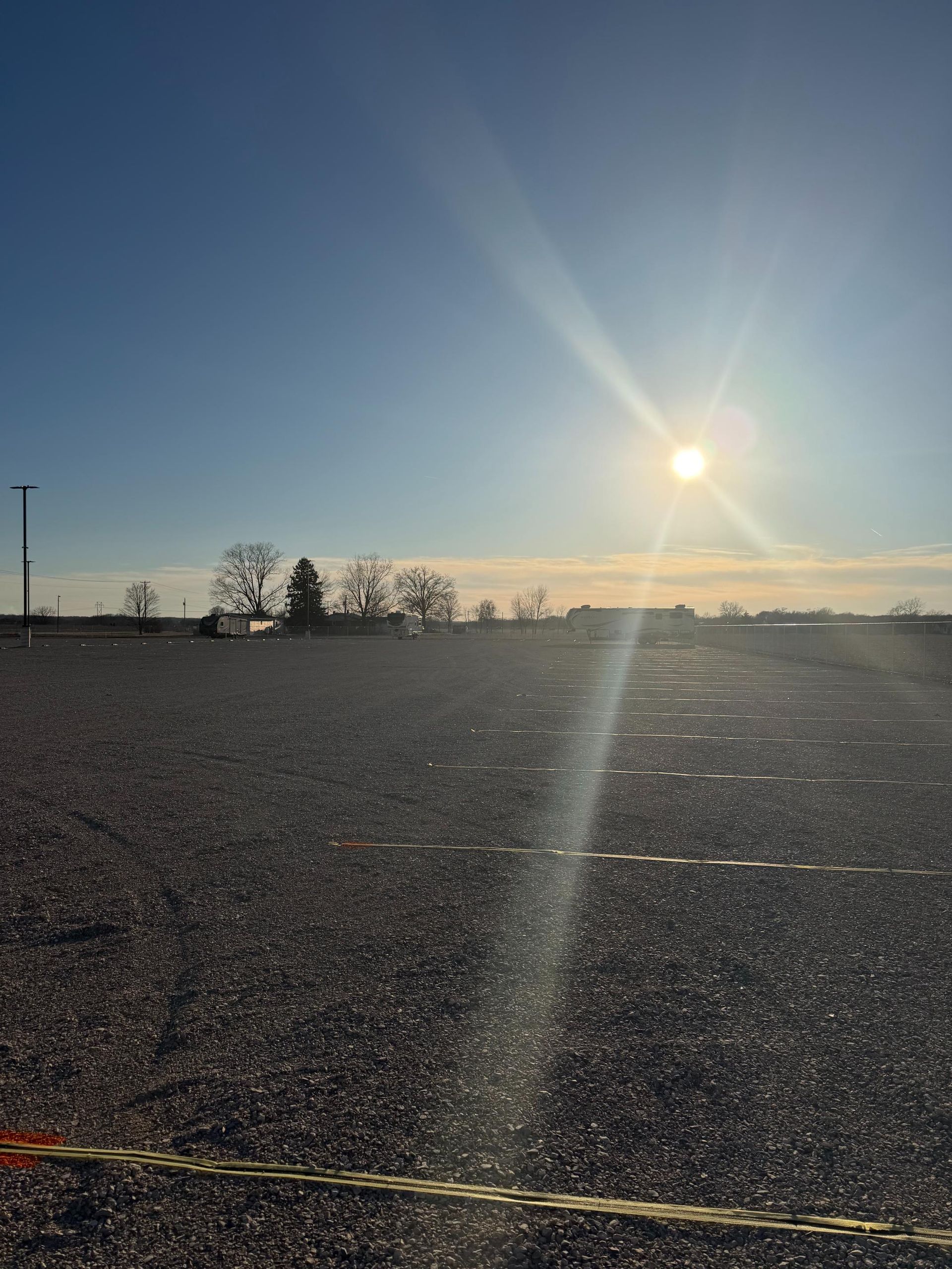 A sunlit gravel parking lot stretching toward the horizon under a clear, blue sky.