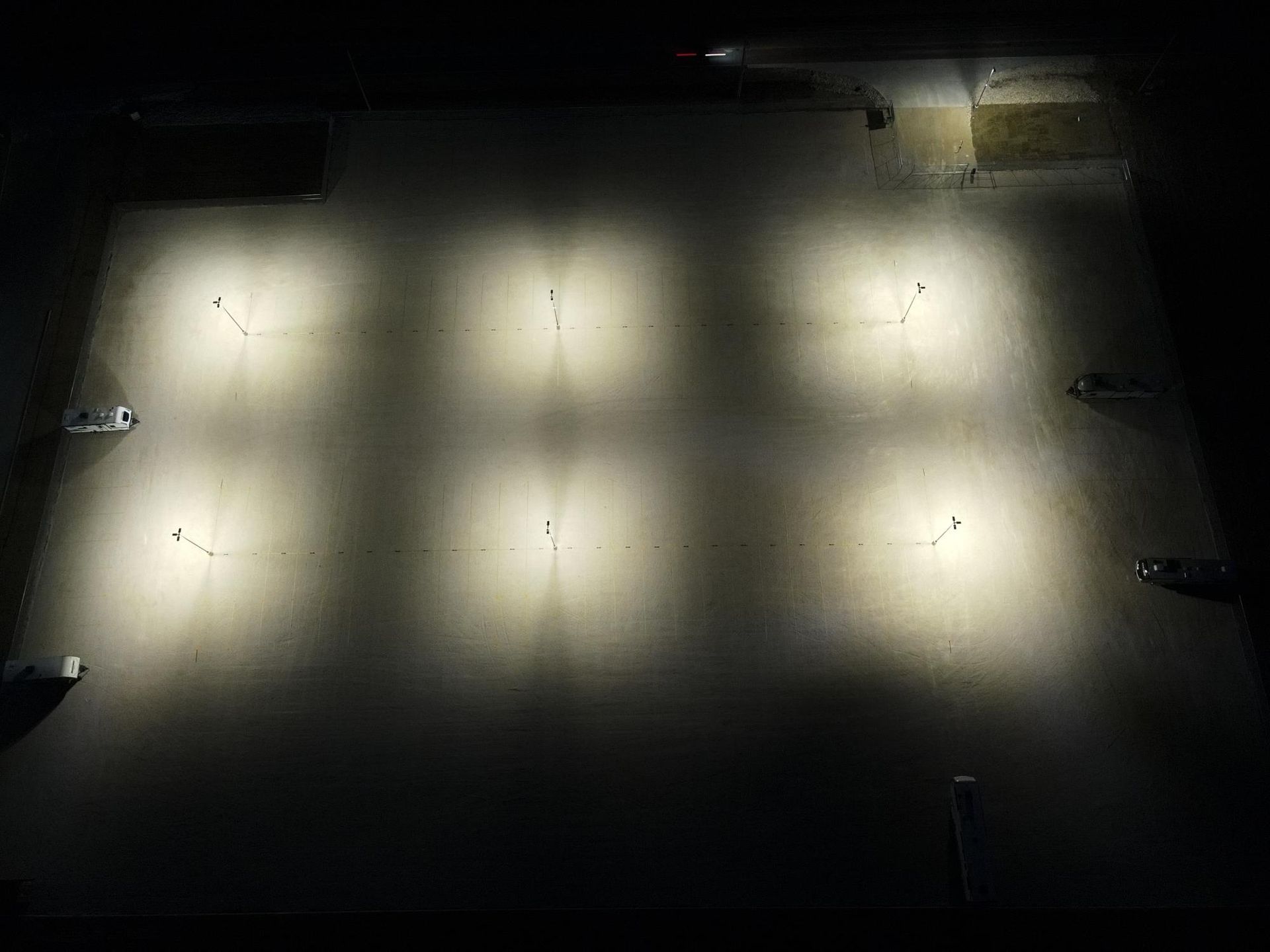 An aerial view of a dark ground lit by six bright, evenly spaced light pools arranged in a grid pattern.