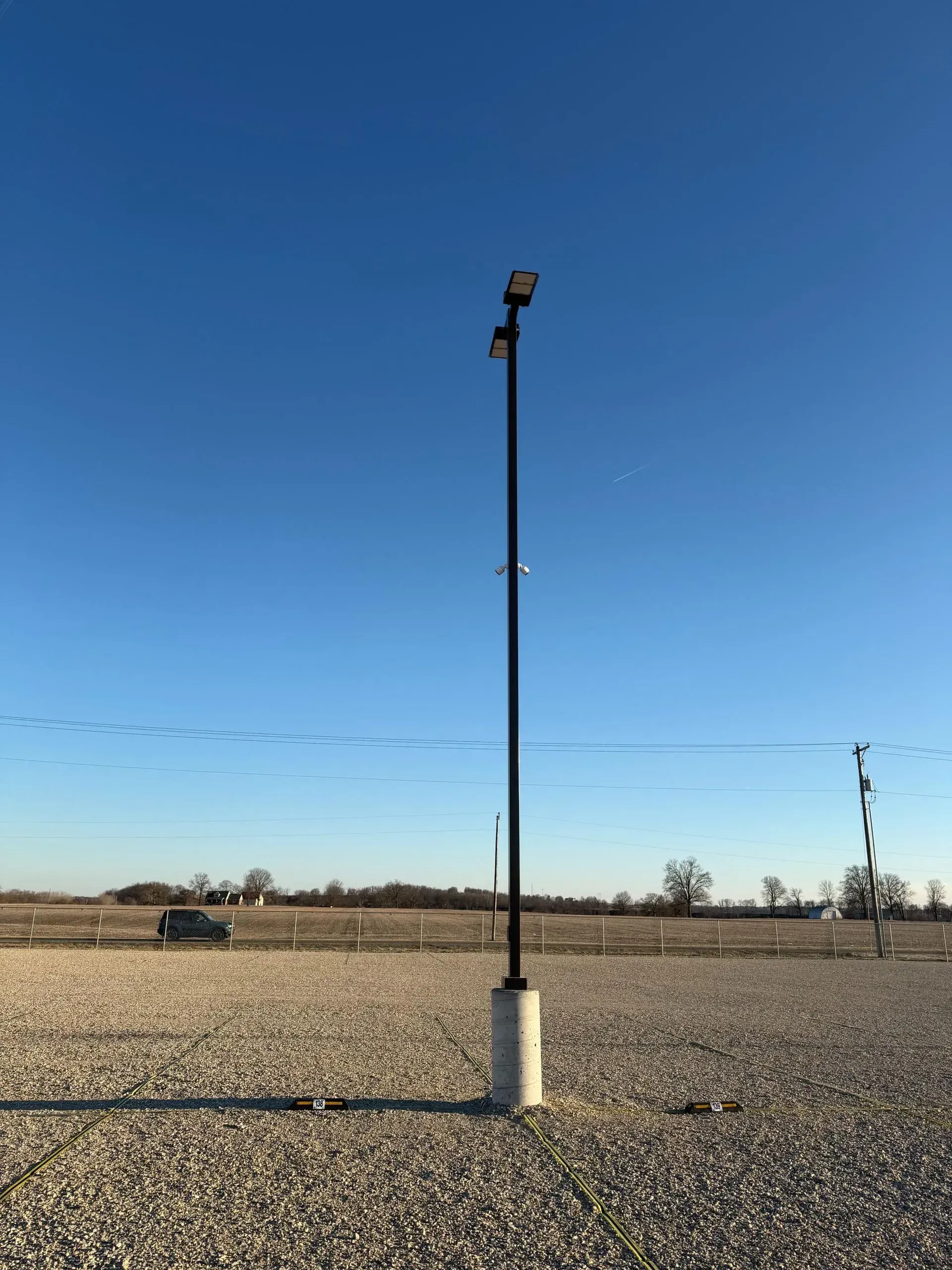 A high pole with security cameras and lights overlooking an outdoor boat storage lot.