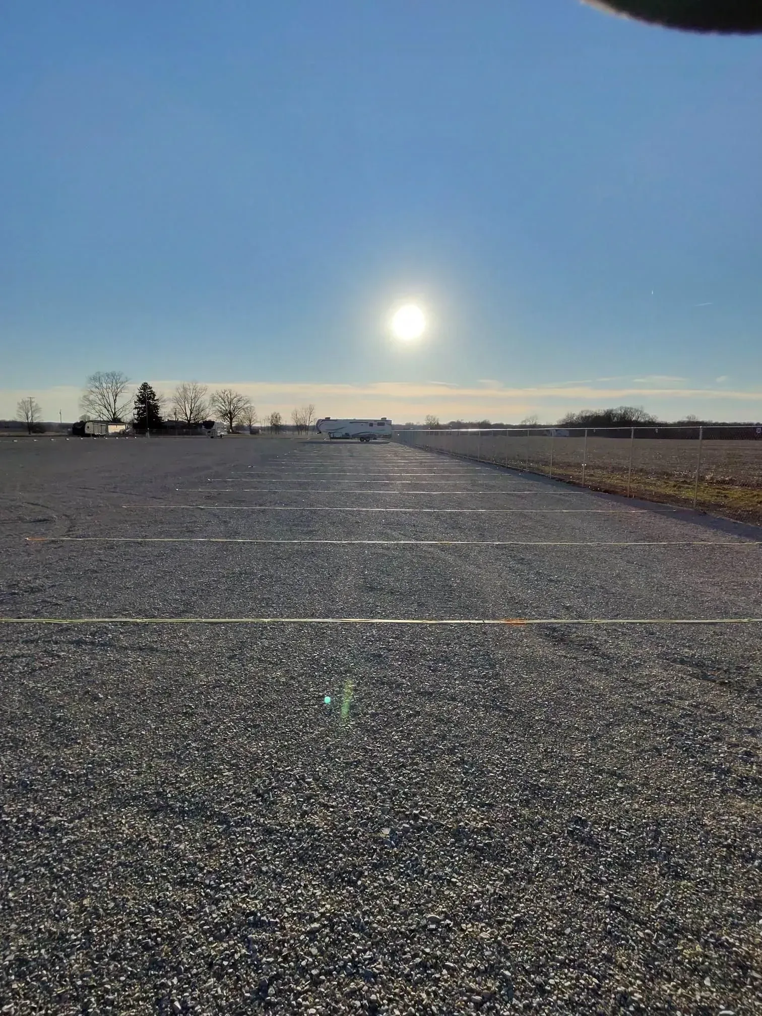 Gravel parking lot with bright sun. Buildings in the distance, blue sky overhead.