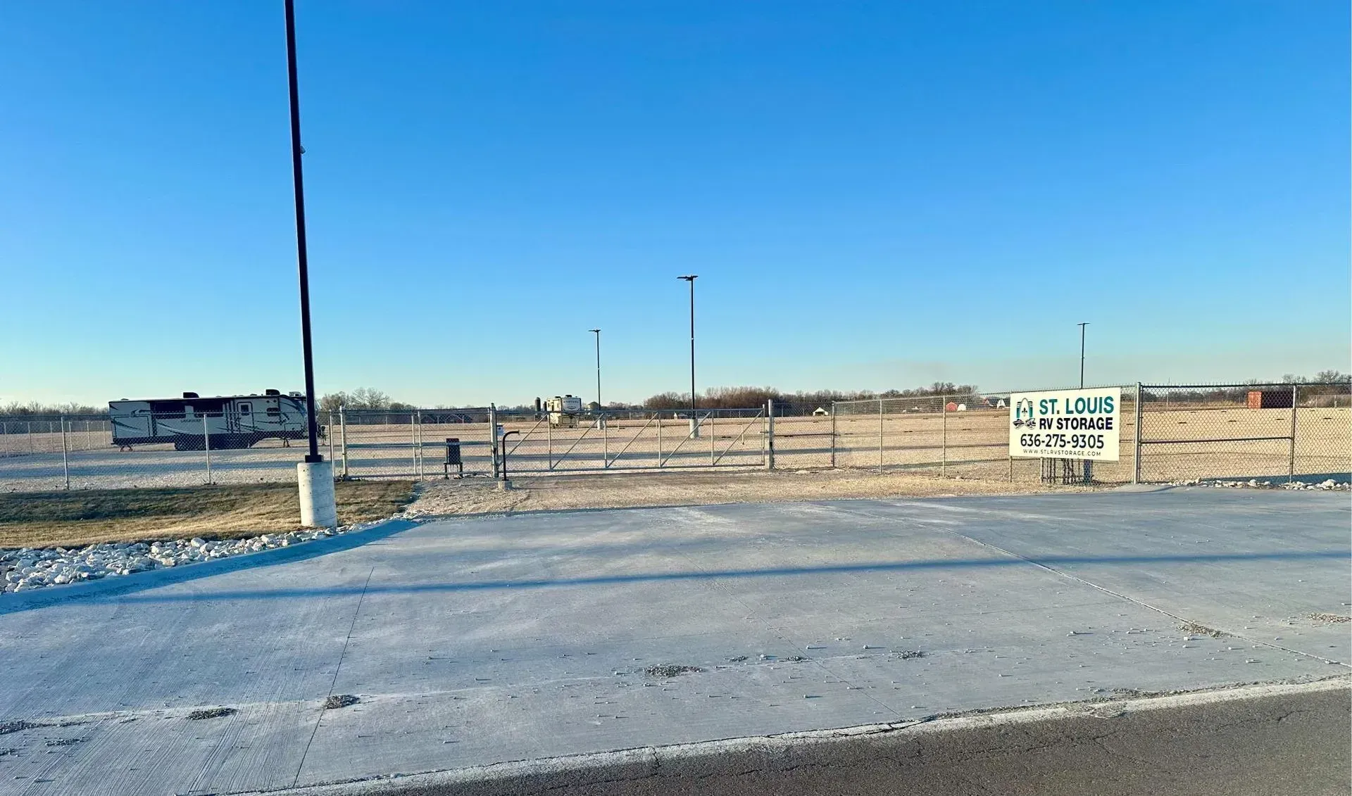 A fenced gravel yard with a St. Louis RV Storage sign, ready for outdoor boat storage.