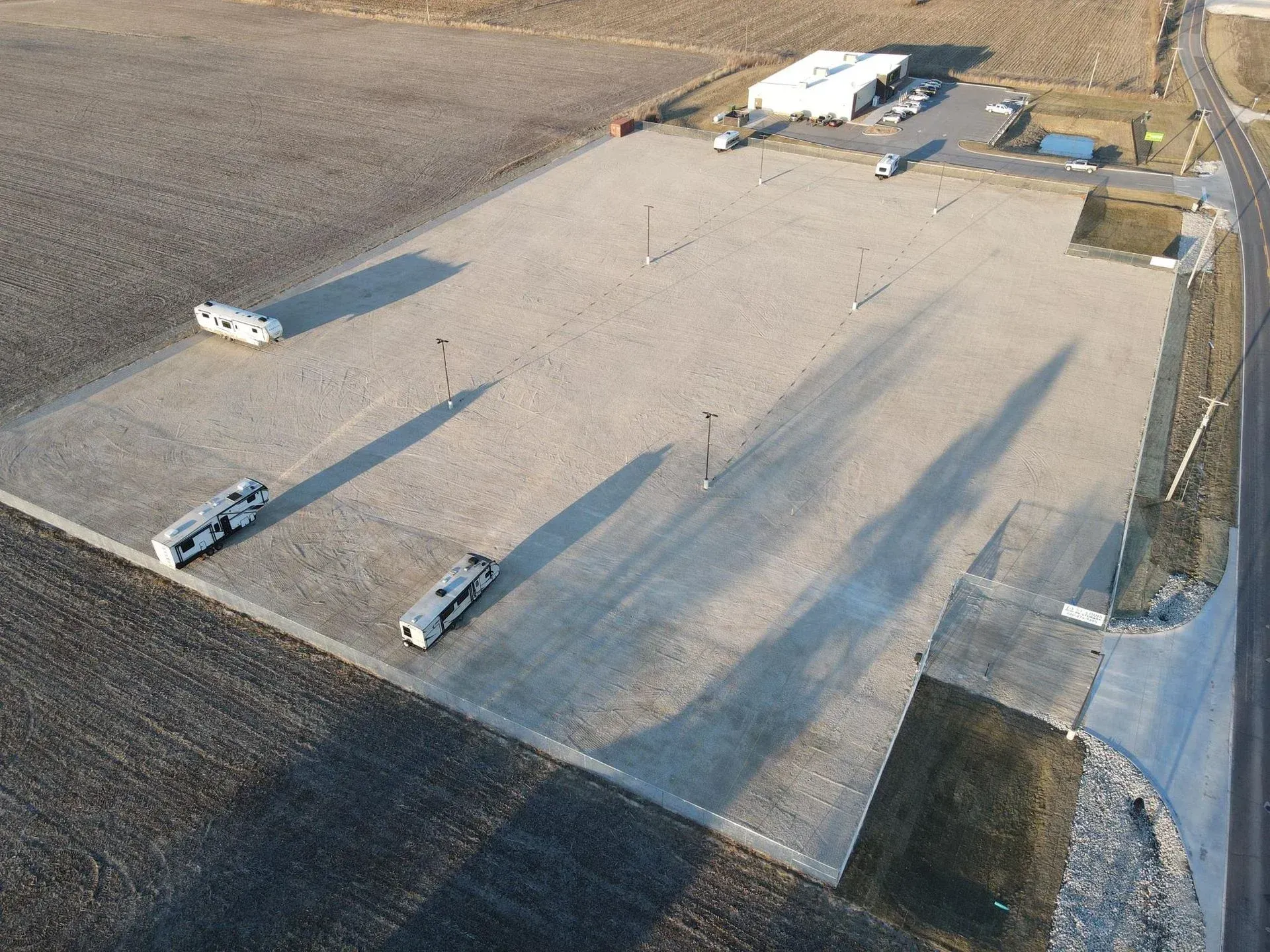 Aerial view of a gravel parking lot with three RVs, shadows, and a building in the background.