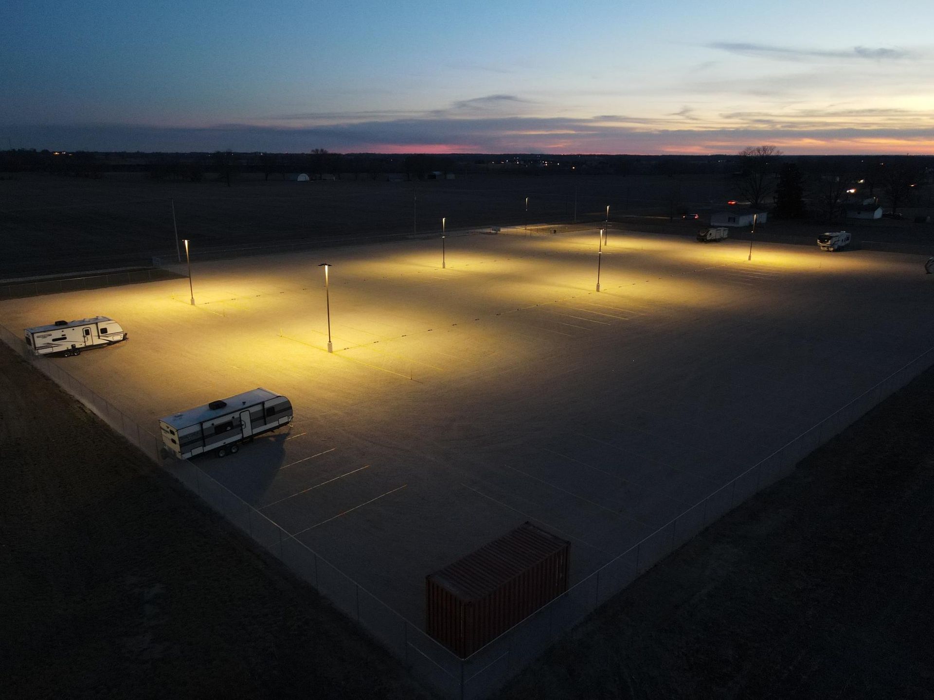 RV parking lot at dusk, lit by overhead lights. Two RVs parked.