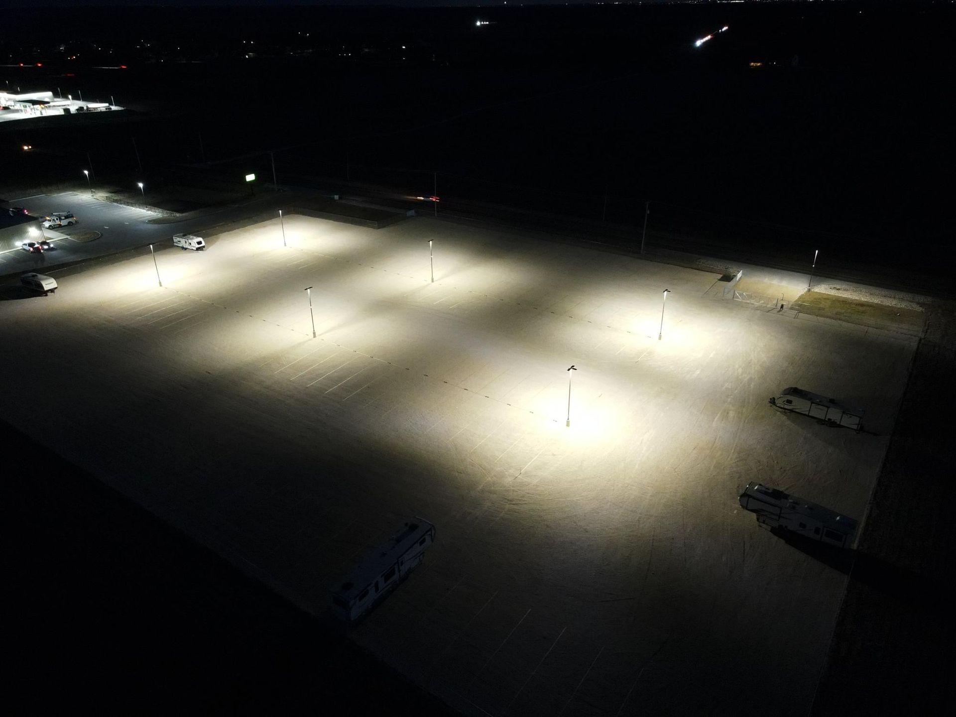 An elevated night view of a large, gravel parking lot illuminated by several bright, evenly spaced light poles.