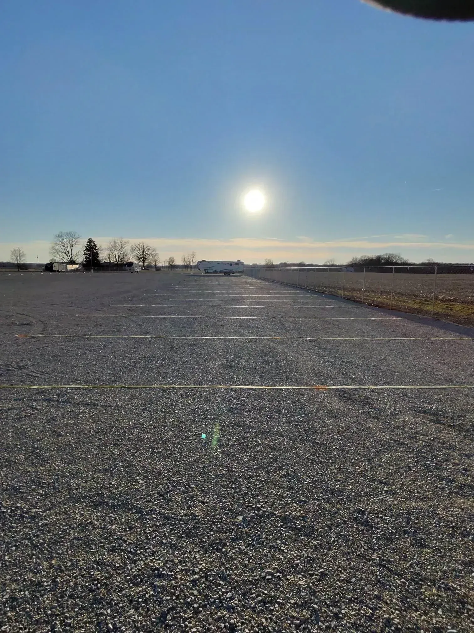 Gravel parking lot under a bright sun. Building in the distance, clear blue sky.