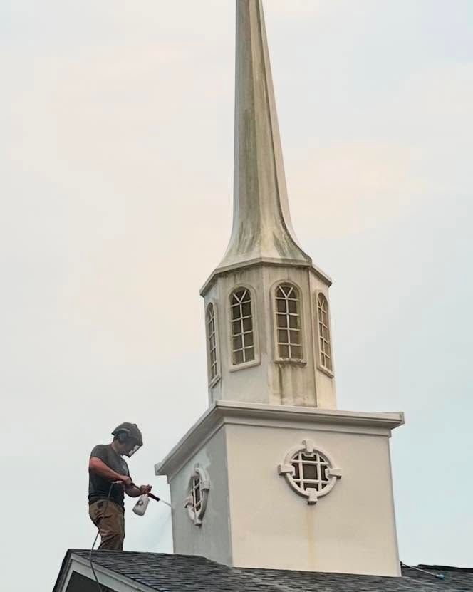 Worker on a church steeple beside a white tower with a tall spire.