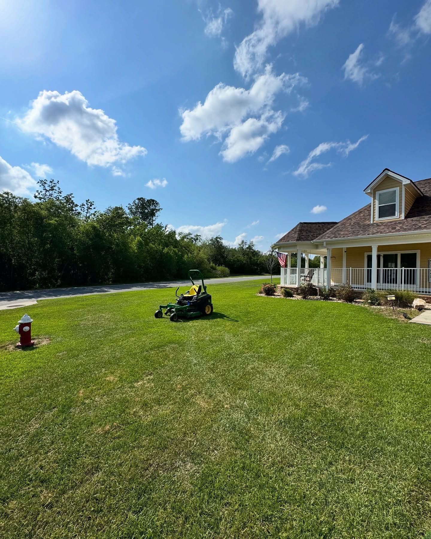 Sunny yard beside a house, with a riding mower on green grass under a blue sky.