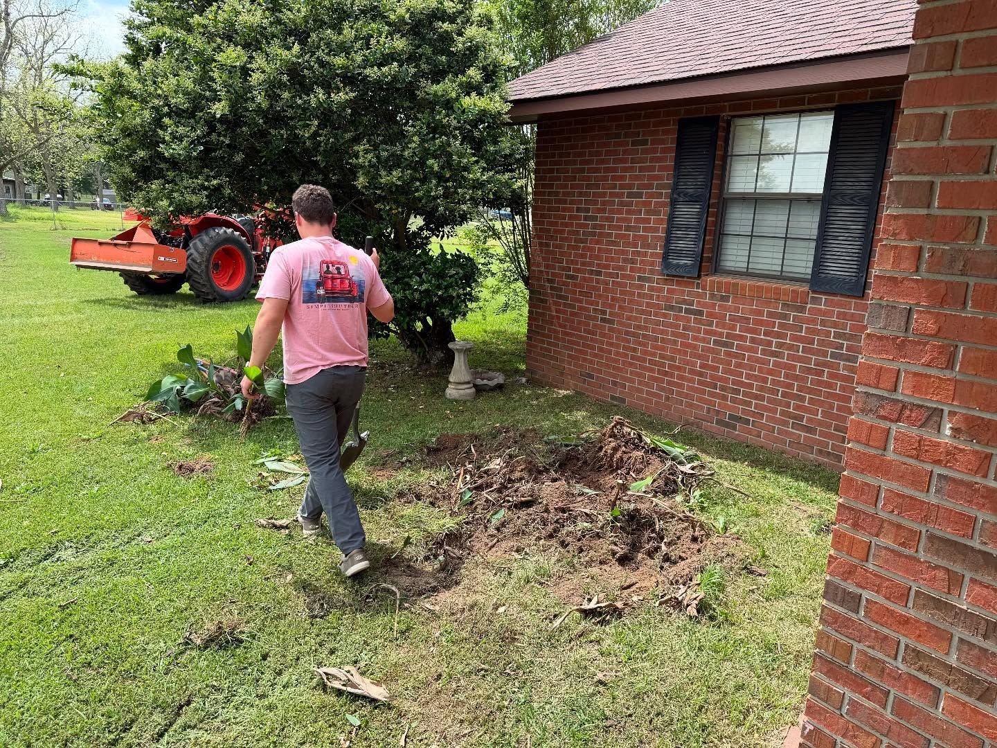 Person walking in a yard near a brick house, with a red tractor and brush pile nearby.