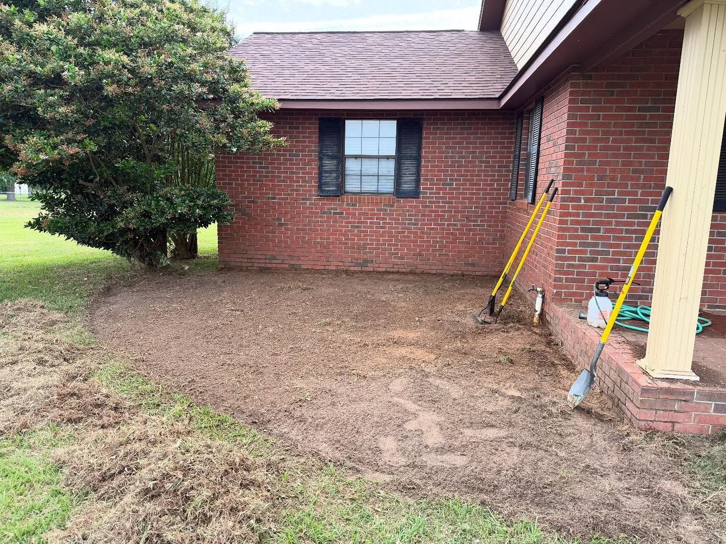 Brick house exterior with small yard, window, and tools leaning against the wall