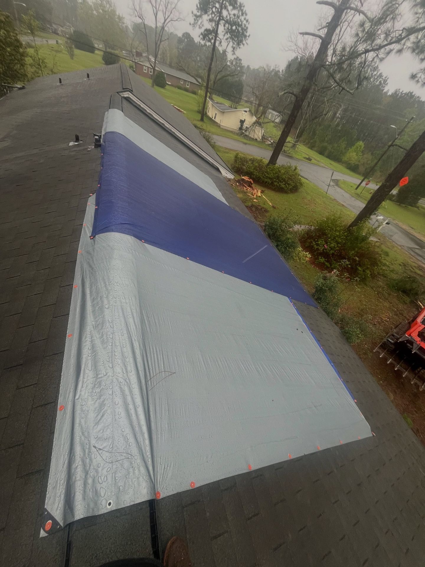 Large blue-and-white sail or tent laid out on a wet paved path in a rainy park