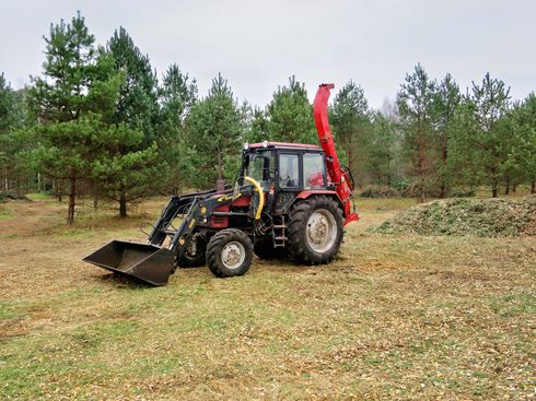 Black tractor with front loader and red backhoe in a grassy field near pine trees