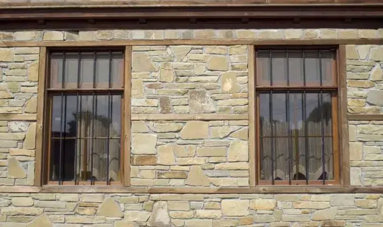 Two Brown-framed Windows With Metal Bars, Set Into a Light-coloured Stone Wall — MJD Roofing Sunshine Coast in Cooroy, QLD
