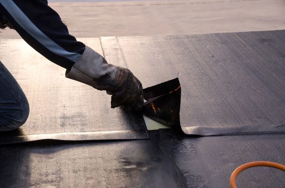 Person in Gloves Applying Sealant to a Black Roofing Membrane — MJD Roofing Sunshine Coast in Sunshine Coast, QLD