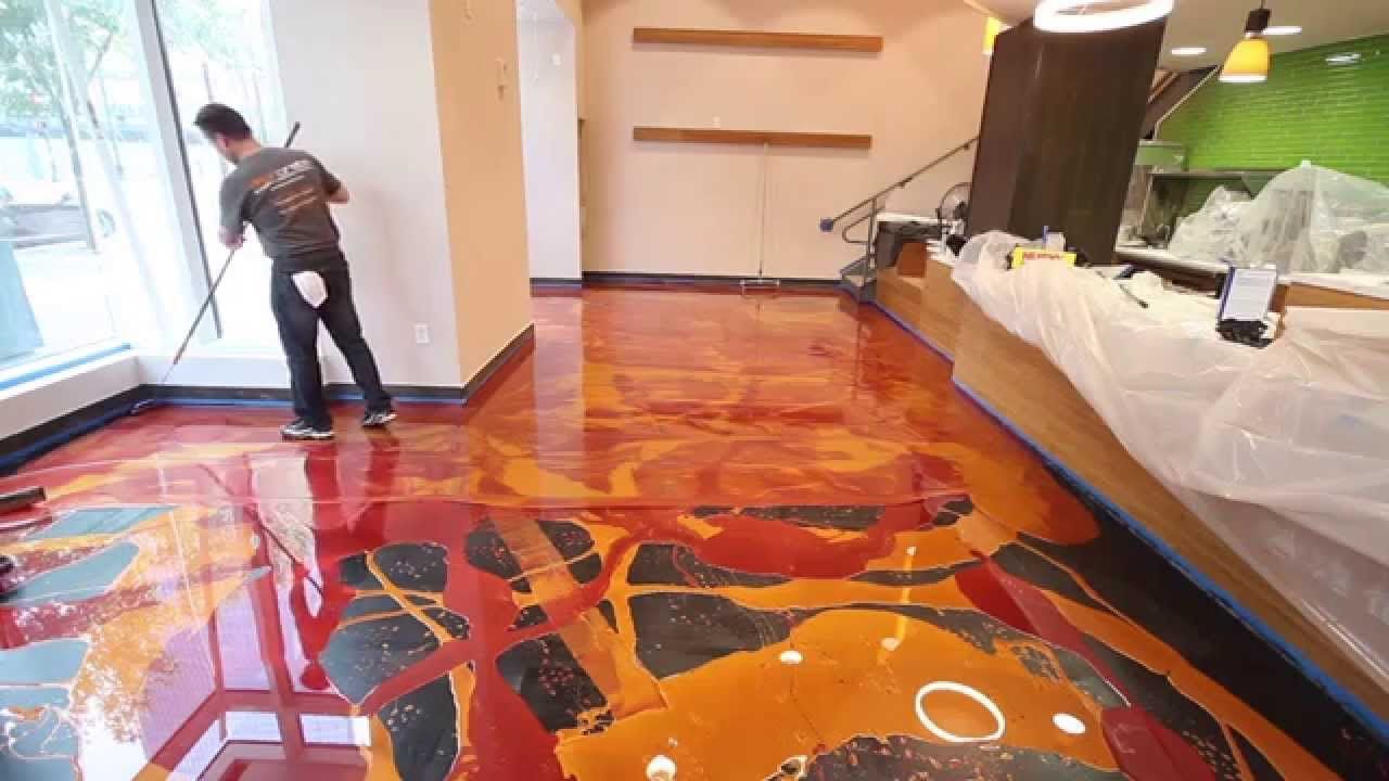 Person painting a glossy floor with bright abstract colors in a room near large windows.