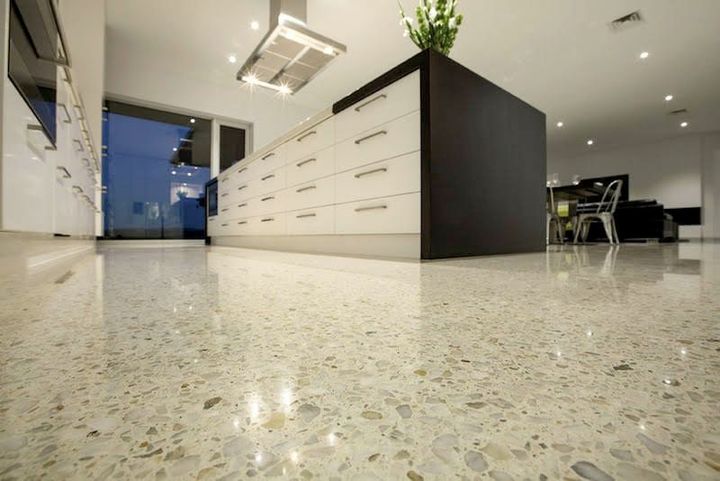 Modern office kitchen with speckled floor, white island cabinets, and black chairs in the background