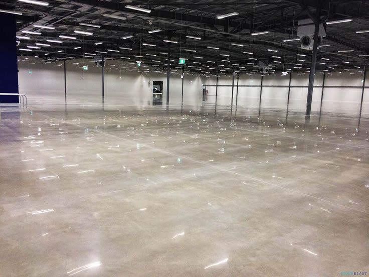 Empty glossy warehouse floor with overhead lights and exposed ceiling beams