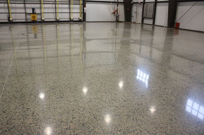 Empty polished warehouse floor reflecting overhead lights and garage doors