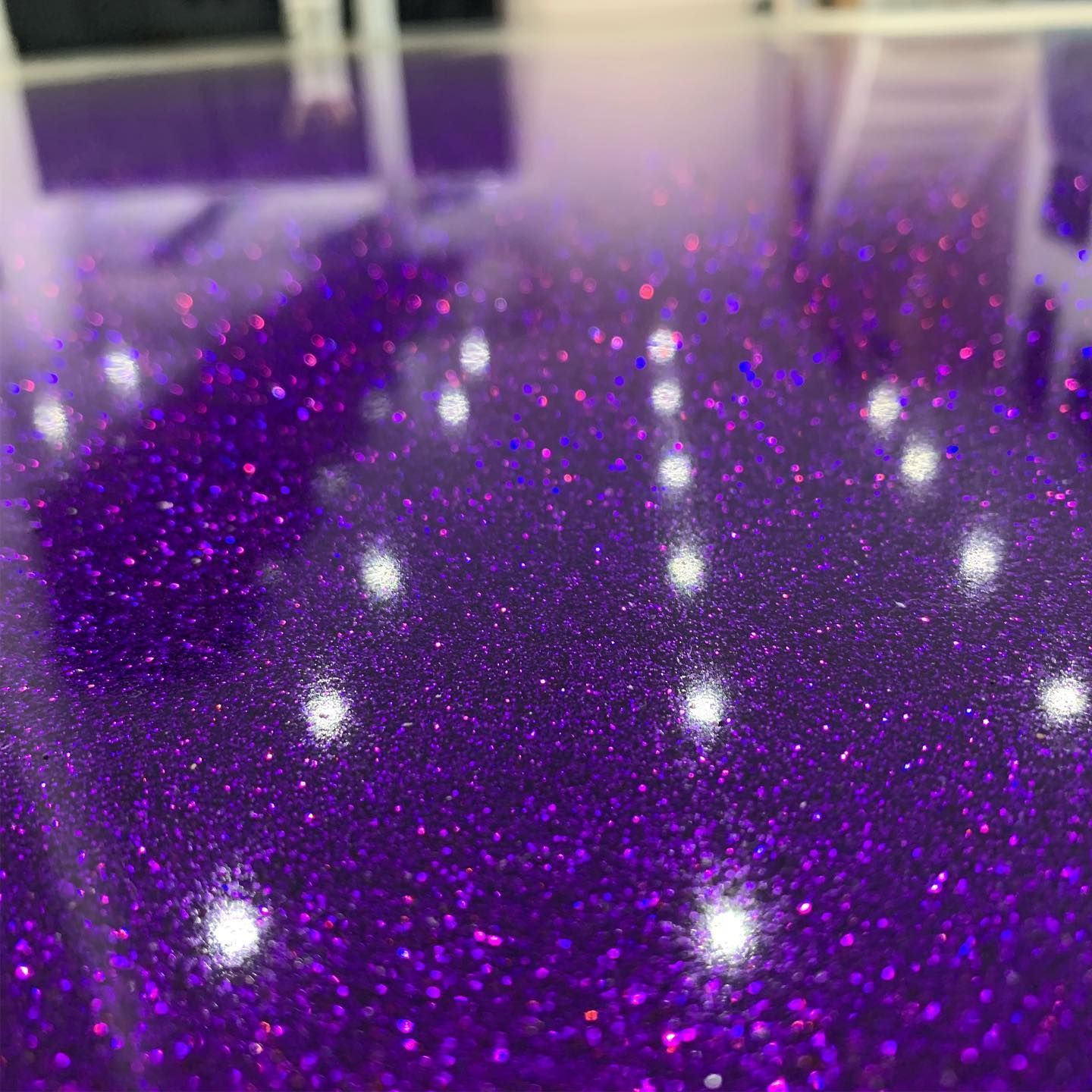 Purple glittery floor with bright white light reflections in an indoor setting