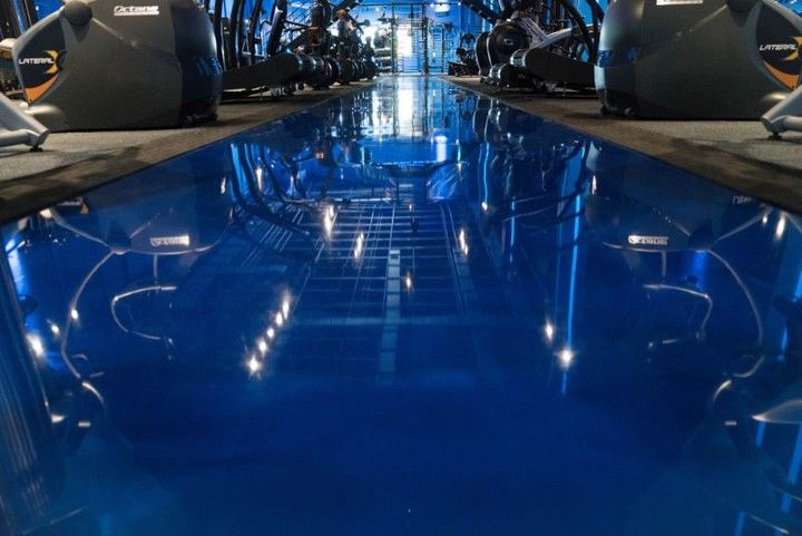 Blue wet floor between race cars in a garage, reflecting overhead lights