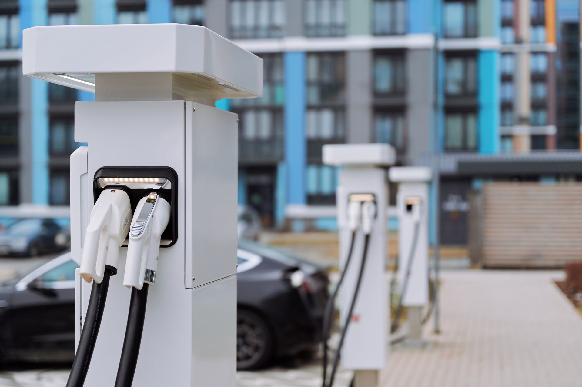 Bornes de recharge pour véhicules électriques devant un immeuble. Bornes blanches avec chargeurs intégrés.
