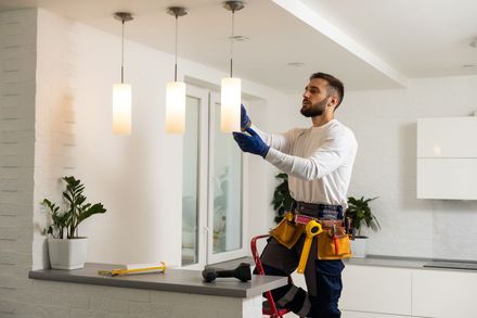 Électricien sur une échelle installant un luminaire dans une cuisine moderne.