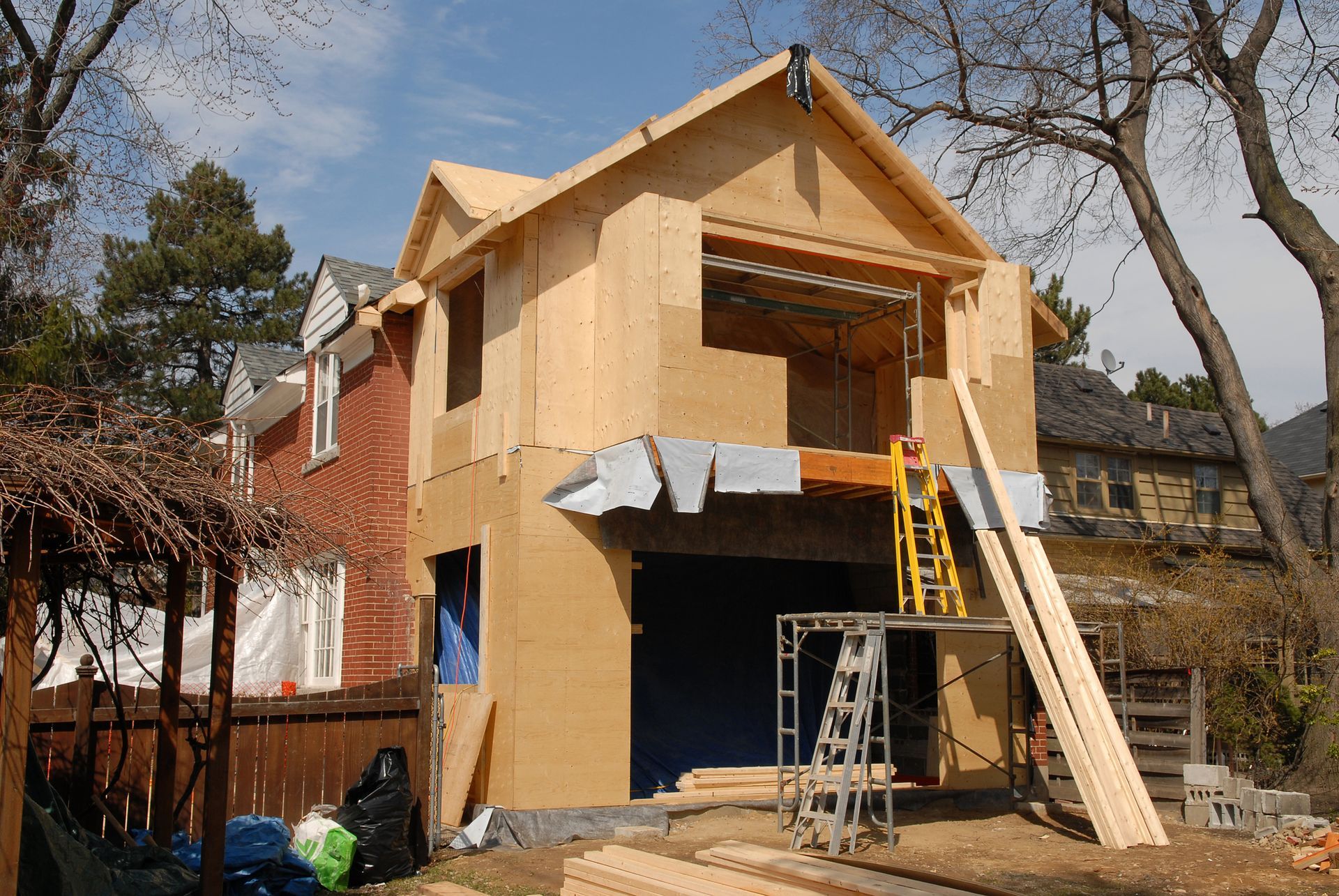 House under construction; wood frame addition to a brick building; ladder and lumber visible.