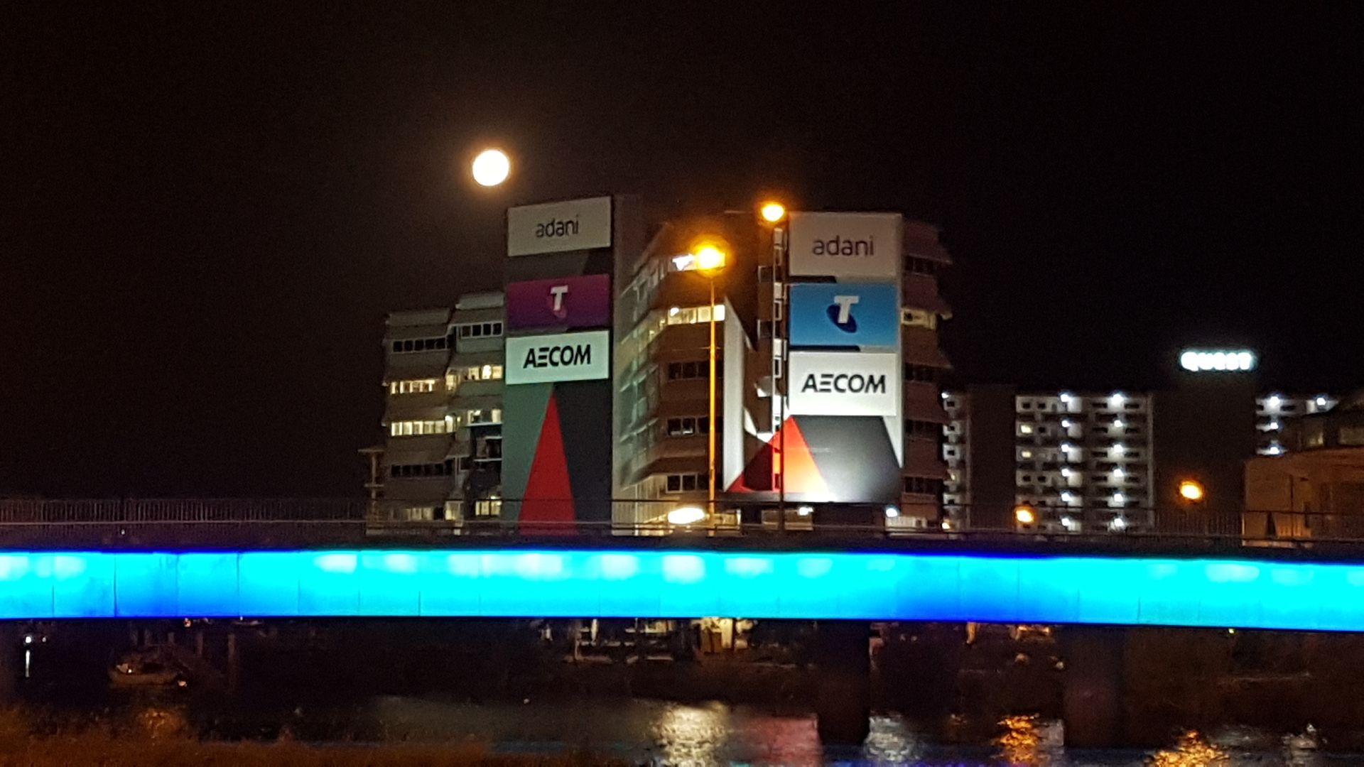 A Bridge is Lit Up With Blue Lighting At Night With Buildings In The Background โ Lex Electrix In West End, QLD