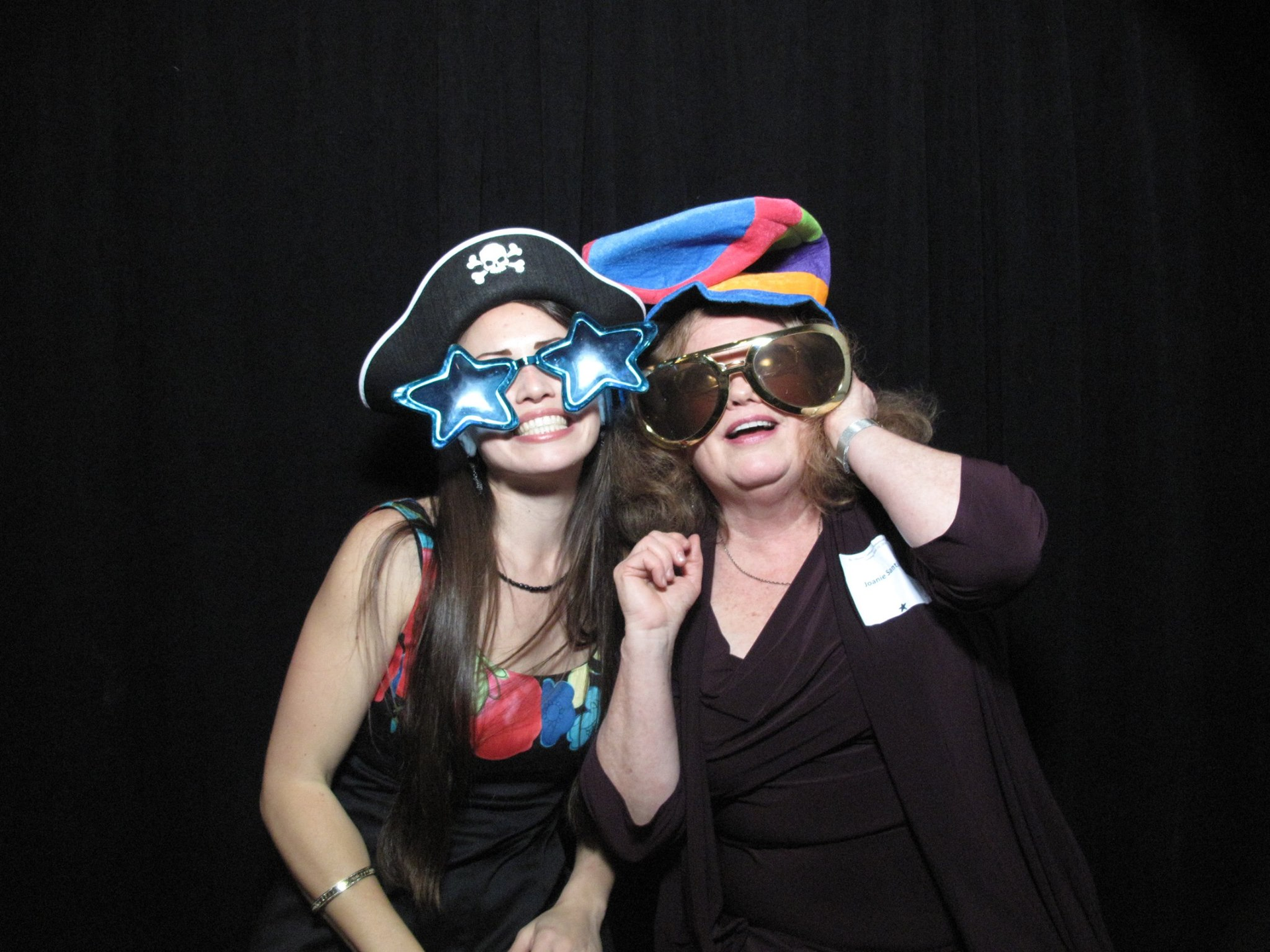 Two people in costumes wearing oversized star sunglasses and colorful hats against a black backdrop