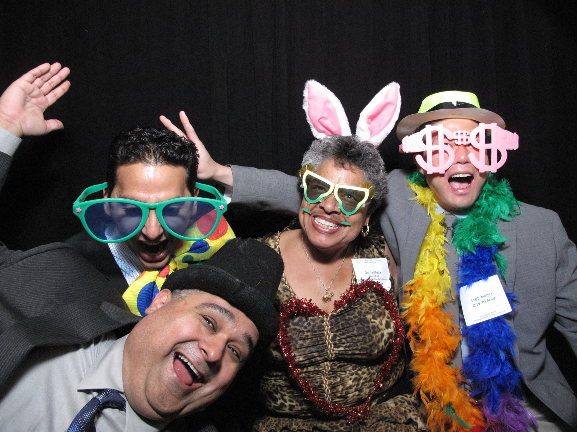 Four people in playful costumes and oversized glasses pose smiling against a black background.