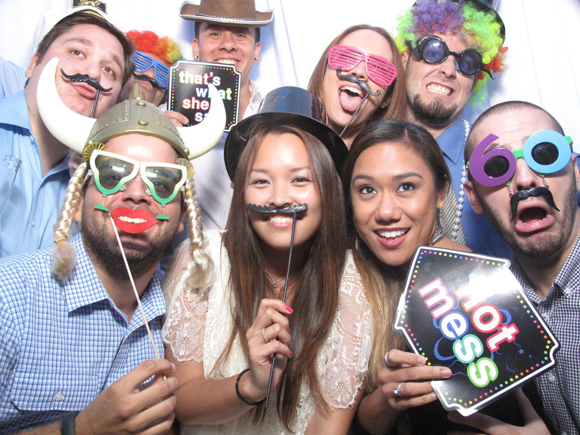Seven people posing in party props with silly glasses and fake mustaches, smiling at the camera.
