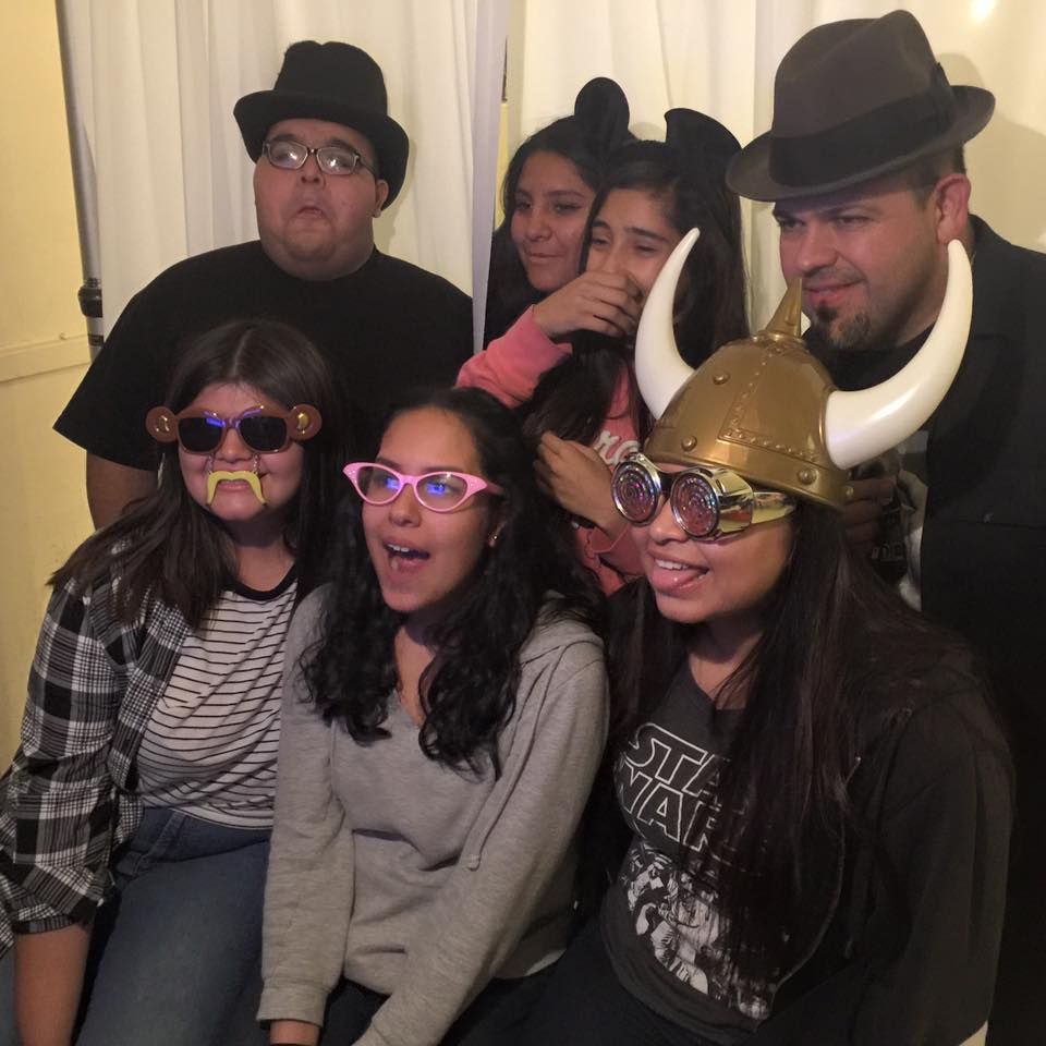 Group posing indoors in hats and novelty glasses, smiling for a playful photo.