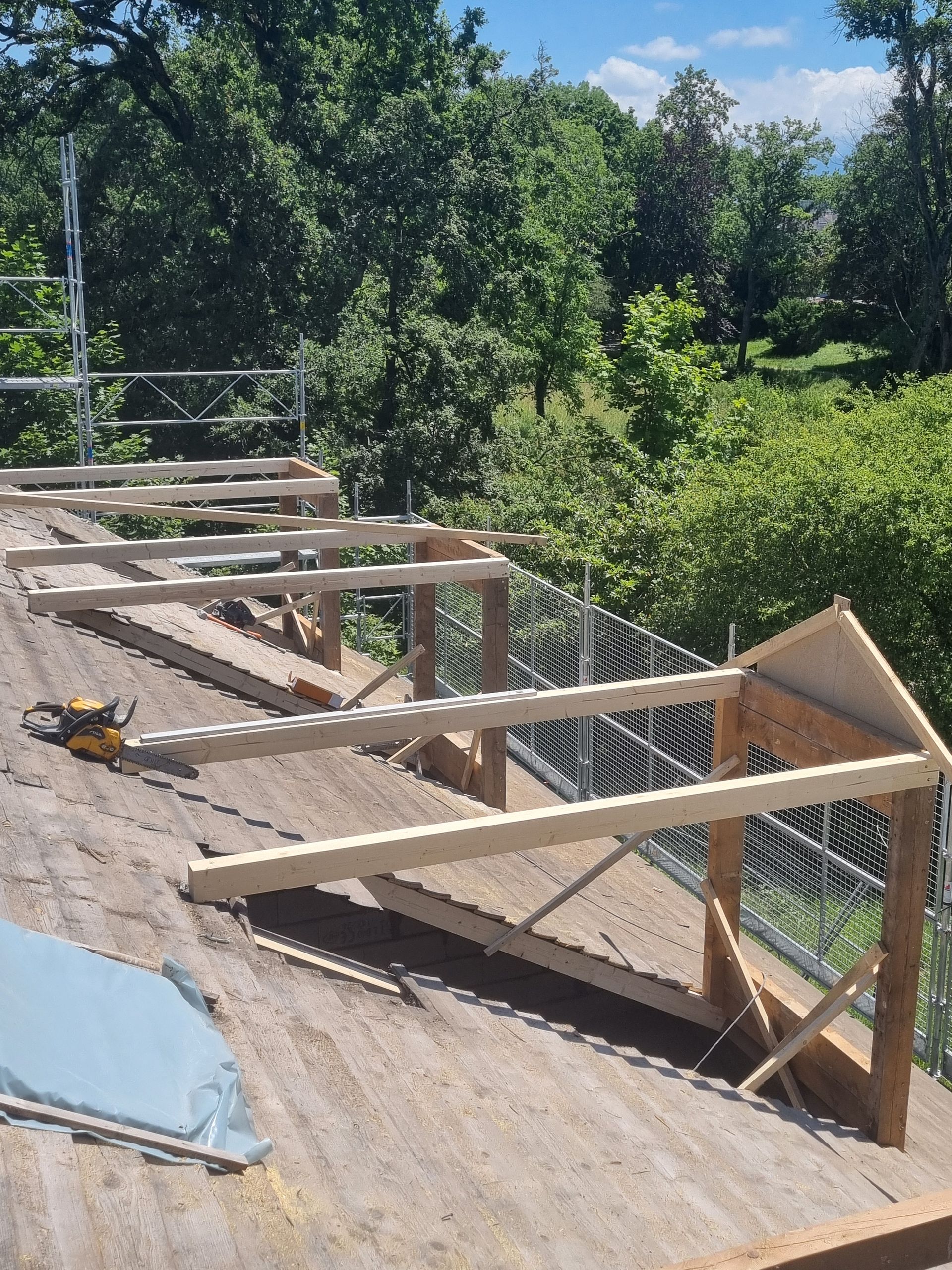 Charpente en bois pour plusieurs lucarnes en construction sur un toit résidentiel en pente recouvert de bardeaux.