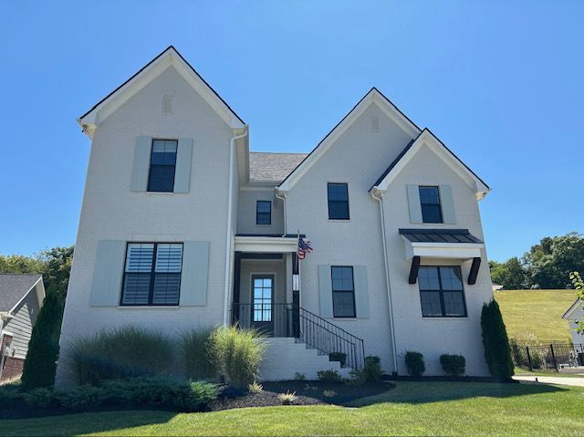 Two-story house with gray stucco, black windows, blue shutters, and a lawn under a blue sky.