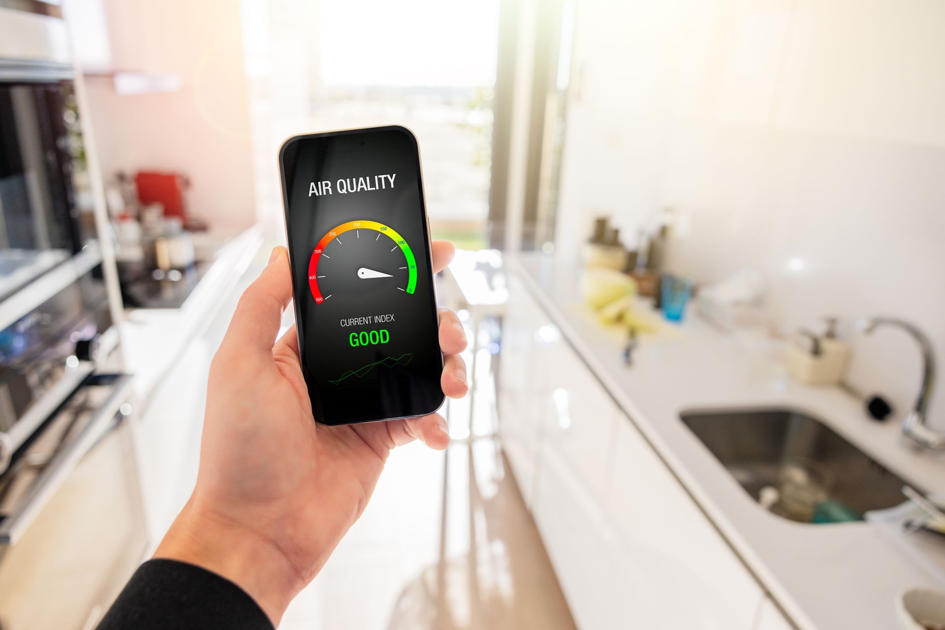 Hand holding a smartphone displaying an energy usage gauge in a kitchen. The gauge is green, and the reading is