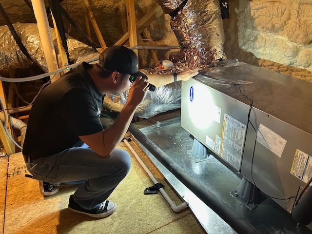 Man inspecting HVAC unit in attic with flashlight.